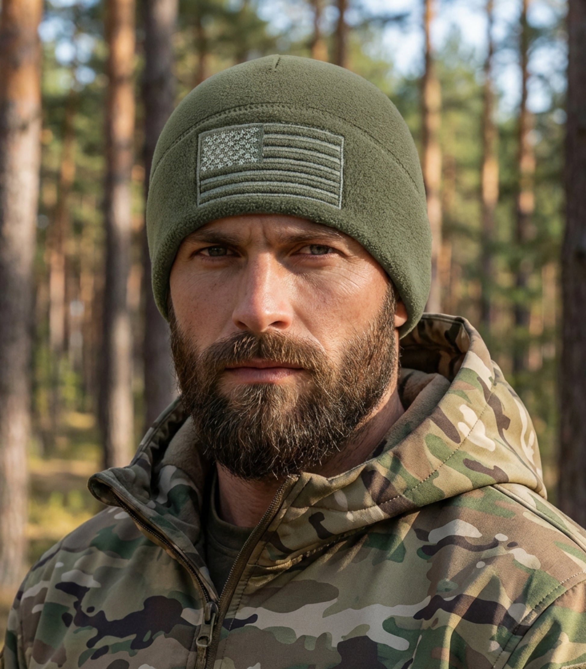 Man wearing a green beanie with an American flag patch and camouflage jacket in a forest setting.