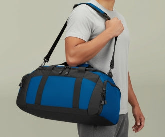 Person carrying a blue duffel bag on a plain background
